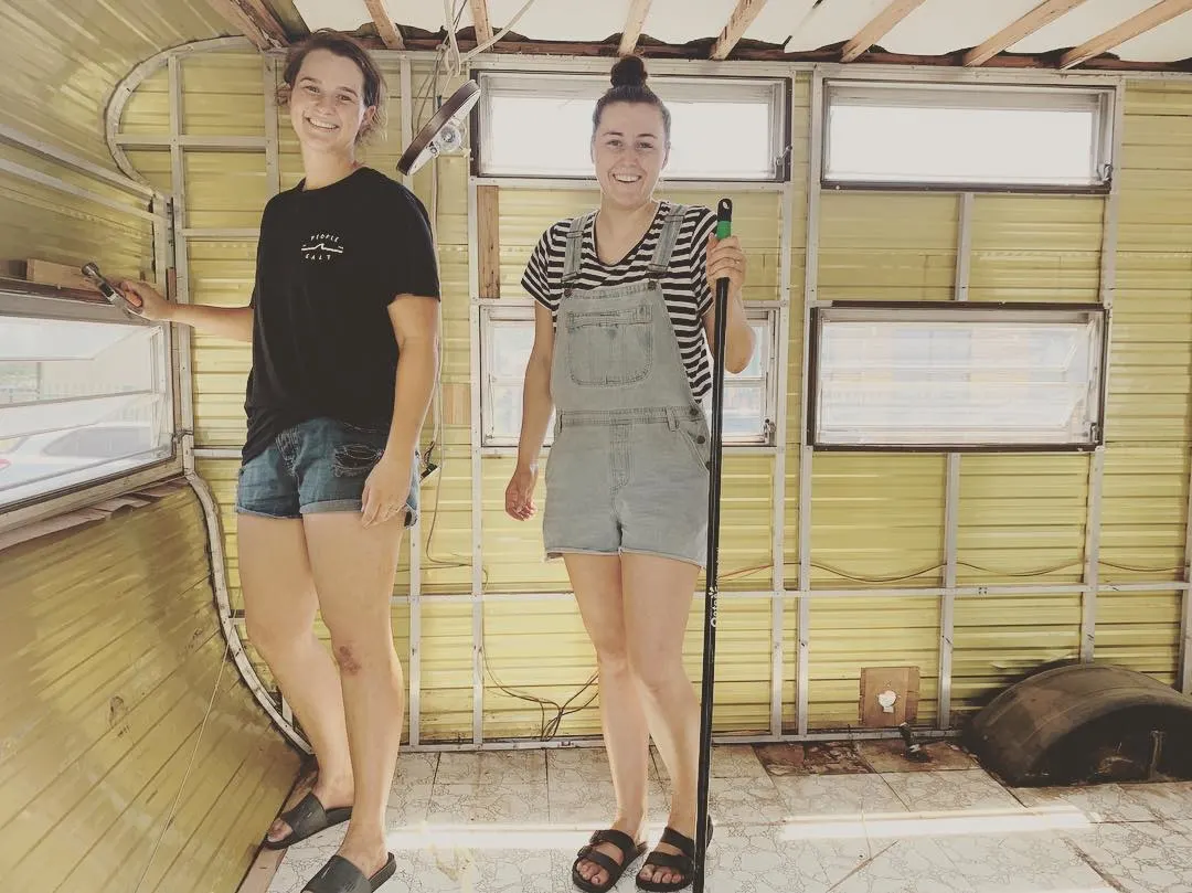 Two women standing inside a gutted vintage caravan