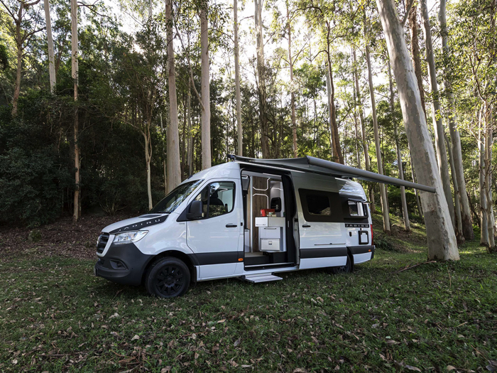 White Trakka Jabiru campervan in a wooded setting, with the awning out and side door open.