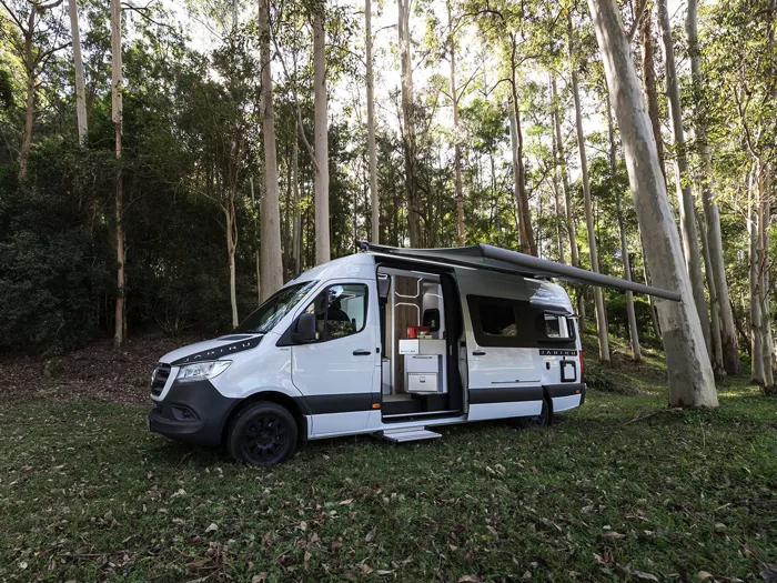 White Trakka Jabiru campervan in a wooded setting, with the awning out and side door open.
