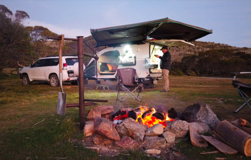 Man beside a campfire with a teardrop camper