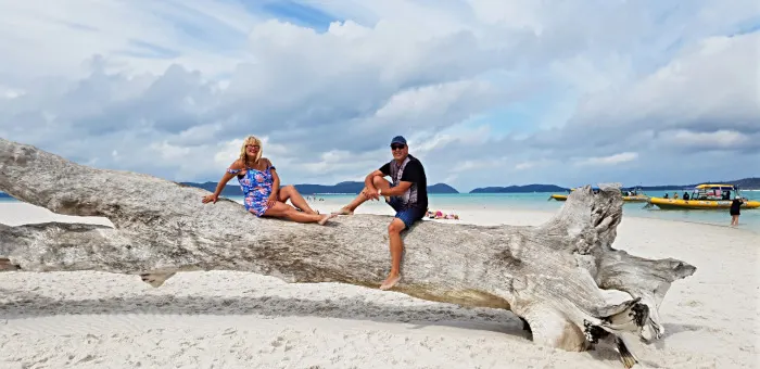 Couple sitting on tree log on white, sandy beach