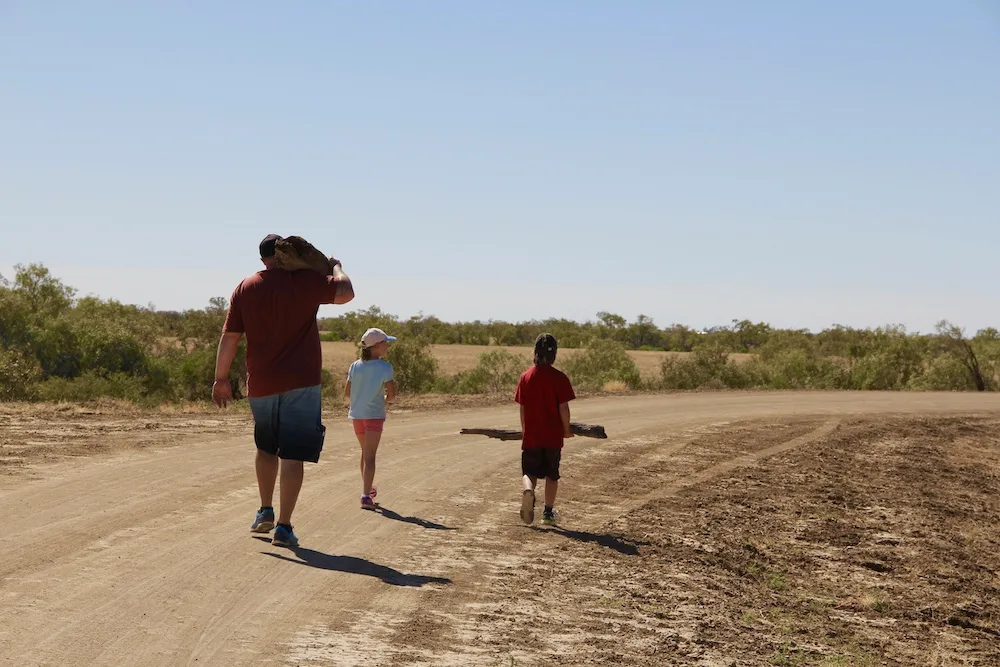 Man and two children walking down a dusty outback Australian road.