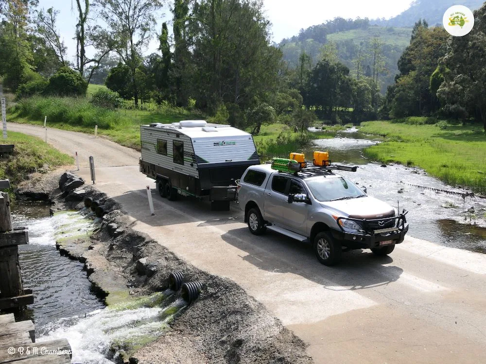 Car and caravan crossing ford across a stream.