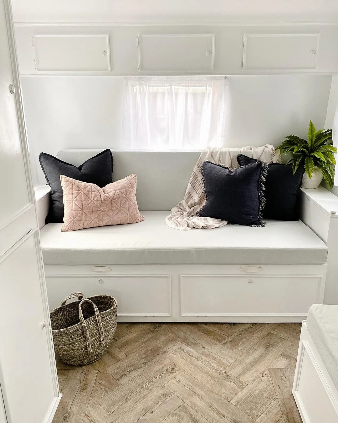 White sitting area with pink and navy blue cushions, in a renovated vintage caravan