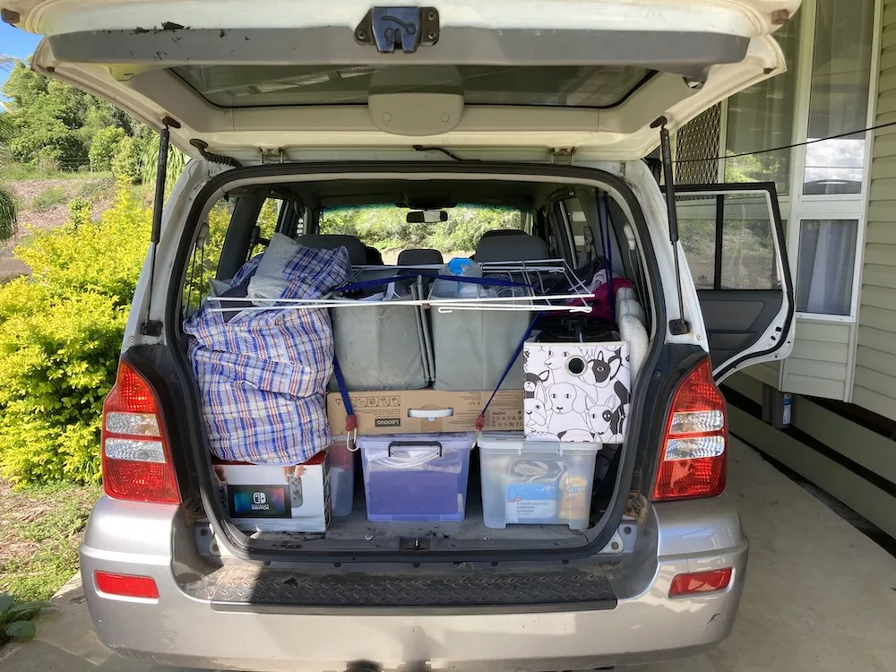 Open rear door of a white SUV, boot is fully packed with boxes and other household items.