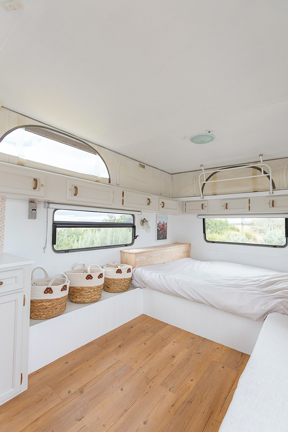 White interior of a renovated caravan showing the bed and storage baskets