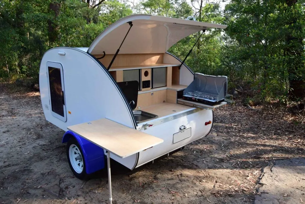 Small, white fibreglass teardrop camper with the rear/kitchen door open.