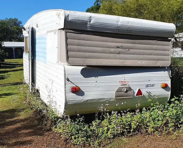 Old caravan in disrepair with grass growing up around it.