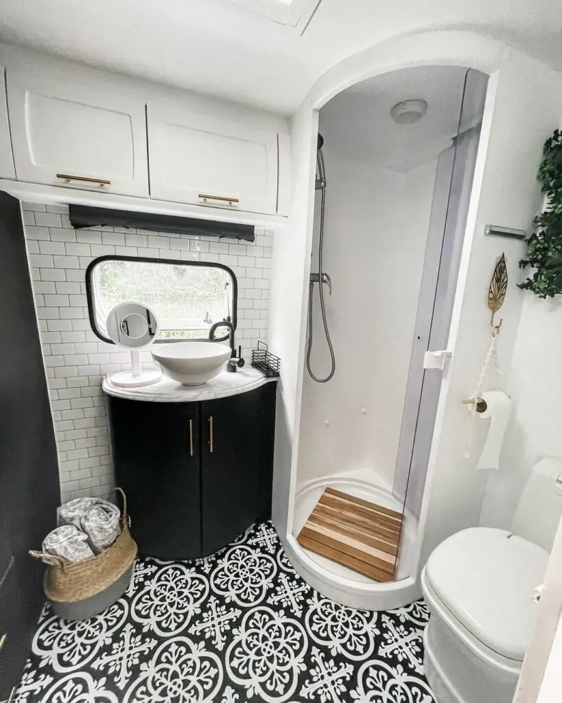 Caravan bathroom after renovation with black cabinets, white walls and shower and black and white floor tiles.