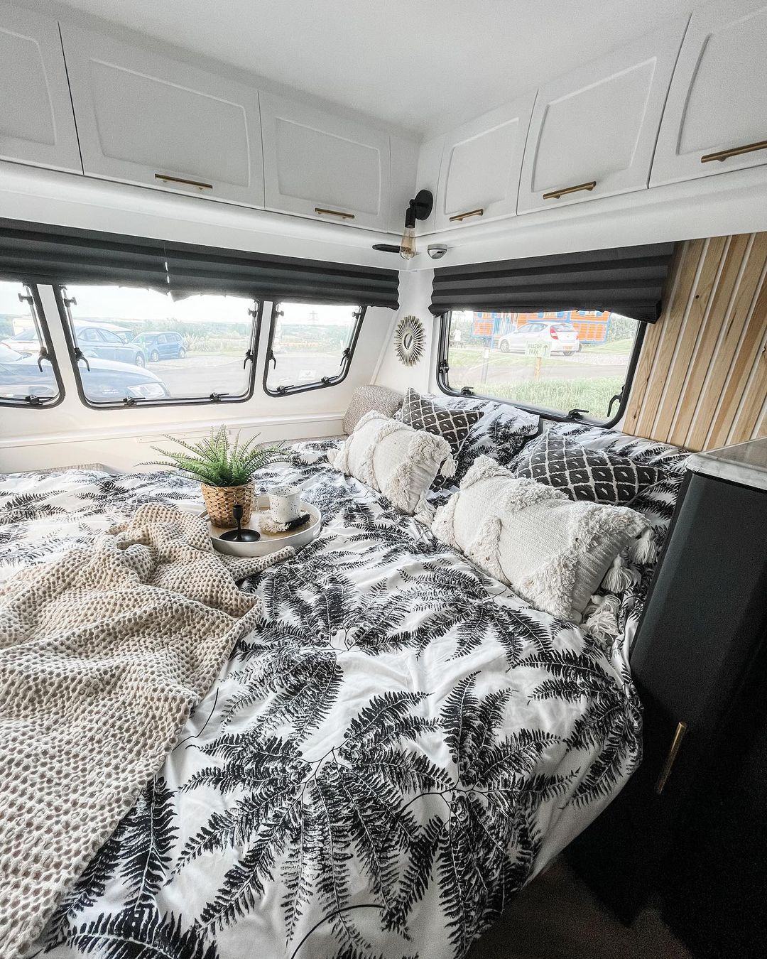 Cozy bed in a caravan with windows surrounding it.