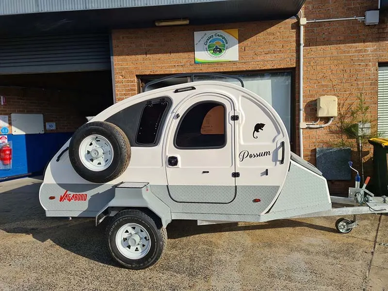 Side view of a white and grey Cruizy Campers teardrop camper parked outside a garage.