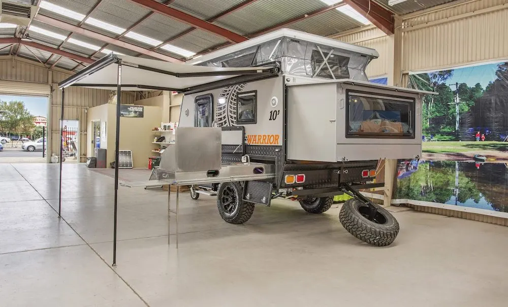 Exterior of a Eagle Campers Warrior 10 hybrid camper showing the awning, kitchen slide and bed extension out.
