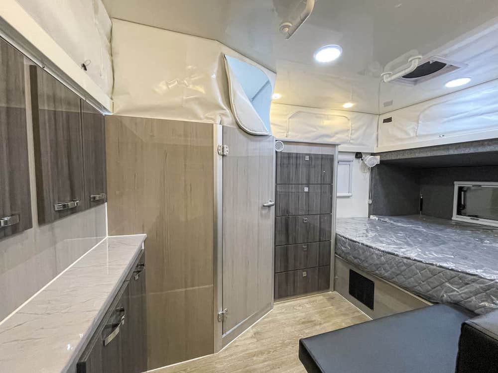 Interior of an empty Prime Campers GT-13C hybrid caravan, showing the bed and living area.