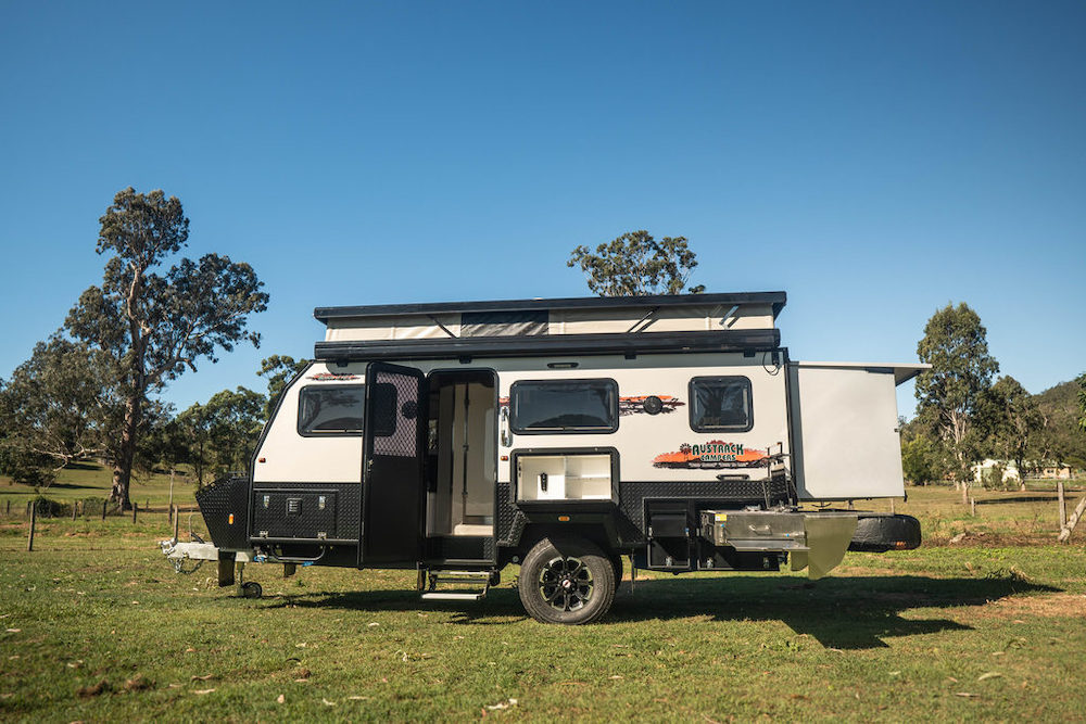 Exterior view of the Austrak Tanami X15L hybrid caravan parked in a green area.