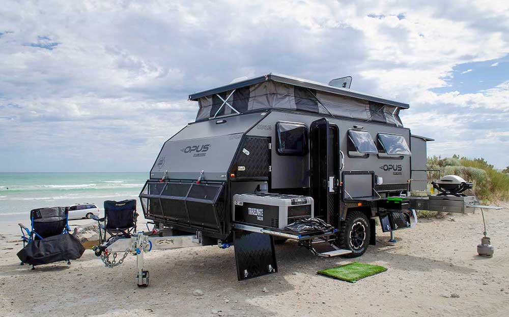 Exterior view of the Opus OP13 hybrid caravan set up at a beach side location.
